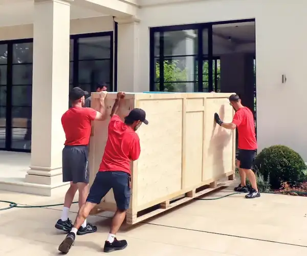 Redpath Moving & Storage team moving a large wooden crate outside a home